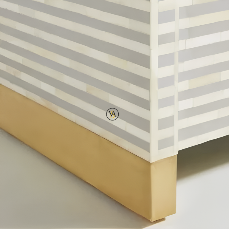 Close-up of the corner of a bone inlay cabinet with horizontal striped white and gray pattern and a brass cladding base