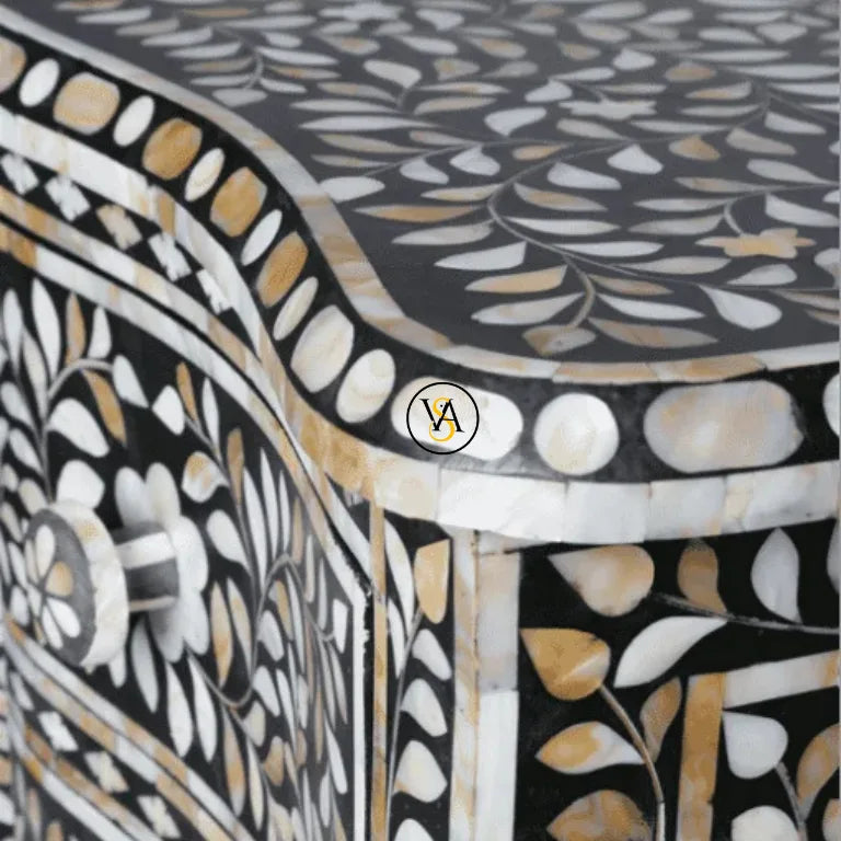 Decorative chest of drawers with intricate black, white, and gold inlay patterns on a dark background.