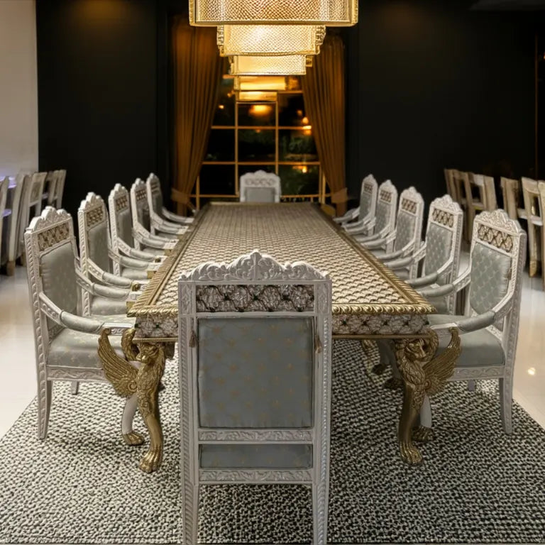 A luxurious mother of pearl dining table with chairs featuring a mother of pearl inlay design on the tabletop, brass carvings on the legs, and teak wood chairs with brass finish on the armrests, lion heads, and carved wings.