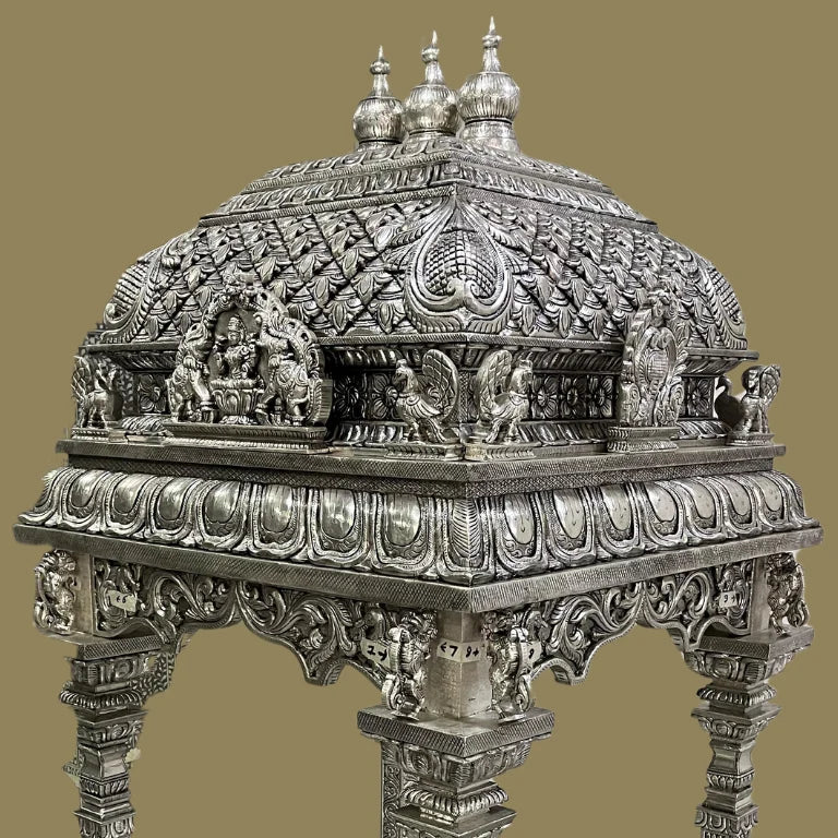 Close-up of white metal temple dome with elephant, peacock, and floral carvings.