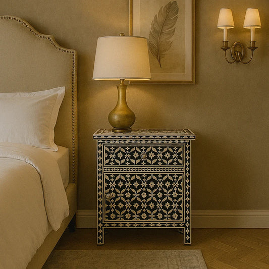 A black side cabinet with bone inlay design, placed next to a bed in a bedroom setting, featuring a lamp and wall sconces in the background.