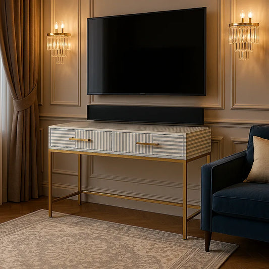 A gray bone inlay console table with two drawers and a brass polished base, placed in a room with a television and wall sconces in the background.