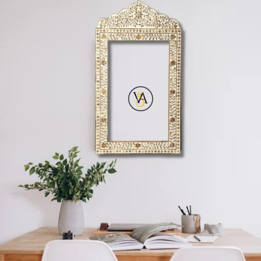 Decorative bone inlay brown mirror frame on a wall above a desk with a plant and stationery items.