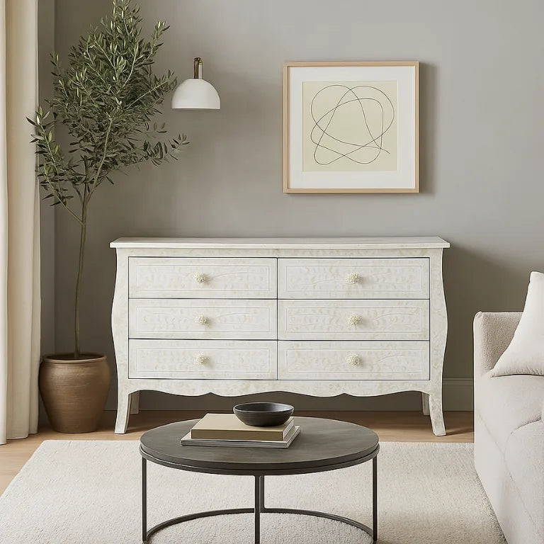 Living room with a bone inlay white 6 chest of drawers , round coffee table, and plant.